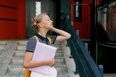 A smiling teenage girl with a backpack and a folder in her hands goes down the stairs