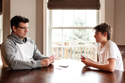 Adolescent boy and his father playing cards at the table together.