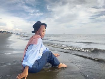 Young woman sitting on beach against sky