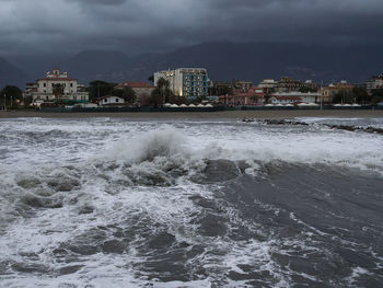 Scenic view of sea and houses against storm clouds