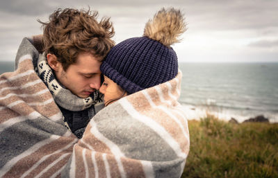 Couple covered with blanket romancing by sea on field