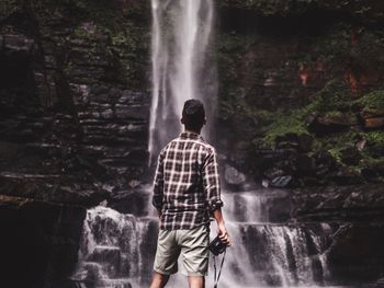 Rear view of man standing by waterfall at forest