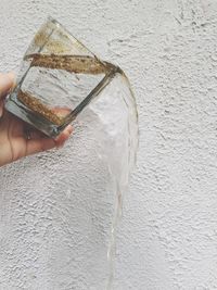 Close-up of hand pouring drink against wall