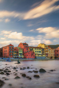 Houses by sea and buildings against sky during sunset