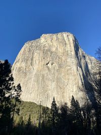 Low angle view of rocky mountain against clear blue sky