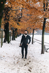 Portrait of handsome man with camera on snow covered footpath during winter