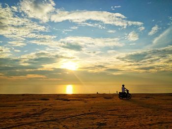 Silhouette man riding bicycle on beach against sky during sunset