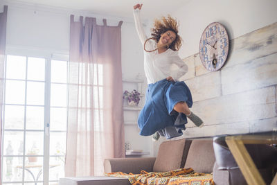 Cheerful woman jumping on sofa at home