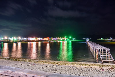 Illuminated city by river against sky at night