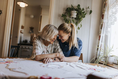 Smiling female caregiver spending leisure time with senior woman sitting at home