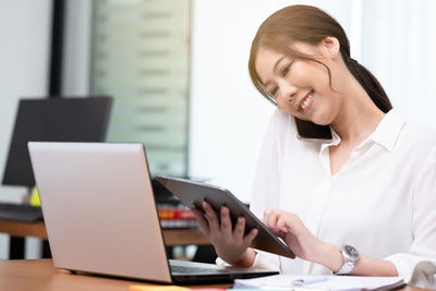 Smiling businesswoman talking on phone while holding digital tablet in office