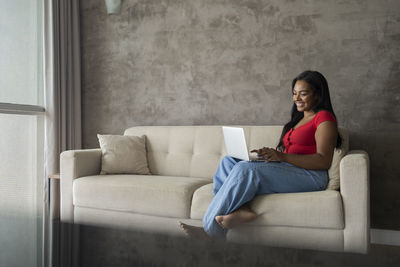 Young black woman working at home with notebook sitting on her couch in the living room. home office