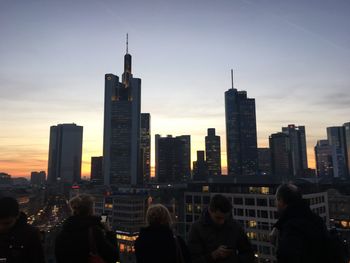 People looking at skyscrapers against sky during sunset