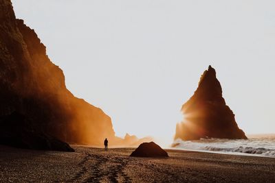 Silhouette person amidst rock formations at beach during sunrise