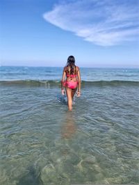 Rear view of teenage girl walking in sea against sky