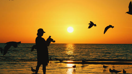 Silhouette couple standing at beach against sky during sunset