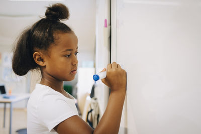 Schoolgirl writing on whiteboard at classroom