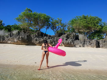 Rear view of woman with inflatable ring walking at beach