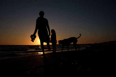 Family with dog walking at beach against sky during sunset