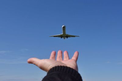 Cropped hand of person reaching airplane against sky