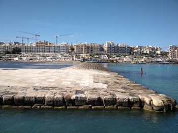 Sea by buildings against clear blue sky