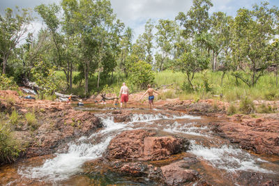 Shirtless people walking on rocks in river