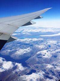 Aerial view of airplane wing over snowcapped mountains against sky