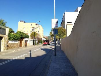 Empty road amidst buildings against clear blue sky