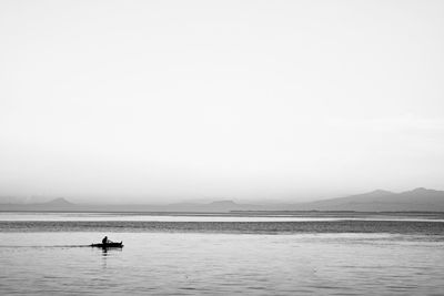 Silhouette person in boat on lake against clear sky