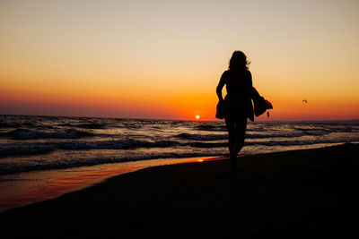 Rear view of silhouette woman walking at beach against clear sky during sunset