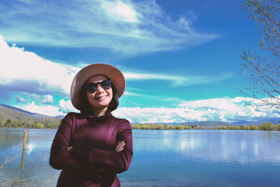 Portrait of woman with arms crossed standing by lake against sky