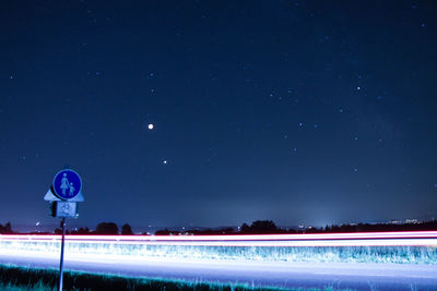 Light trails on road against blue sky at night