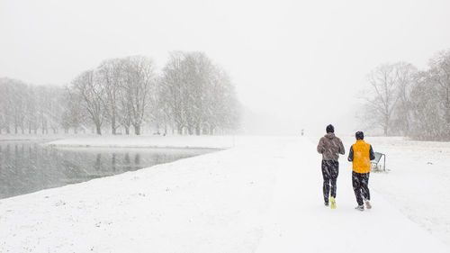 Rear view of people jogging on snow covered landscape