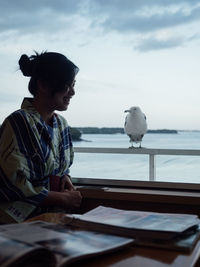 Smiling woman looking at seagull perching on railing