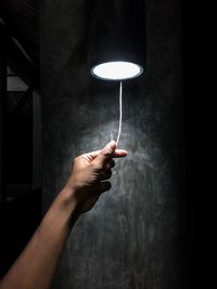 Cropped hand gesturing under illuminated lighting equipment hanging indoors