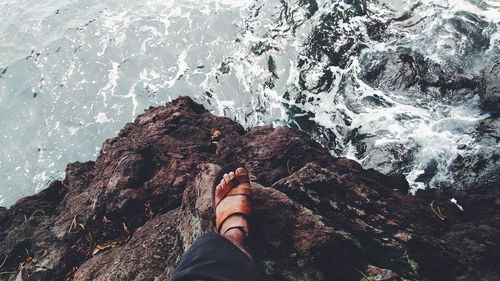 Low section of man standing on cliff by sea