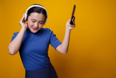 Mid adult man using smart phone against yellow background