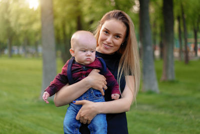 Portrait of smiling mother carrying cute son in park