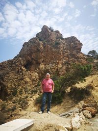 Portrait of man standing on rock against sky