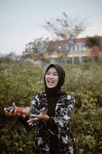 Young woman holding bottle while standing against plants