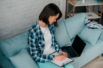 Young woman using laptop while sitting on sofa