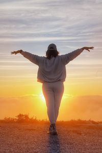 Rear view of woman standing at sunset