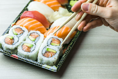 Cropped hand having sushi and sashimi in box on table