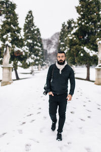 Portrait of handsome man with camera on snow covered footpath during winter