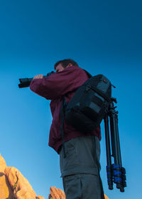 Low angle view of man photographing against blue sky