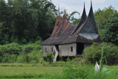 House on field by trees against sky