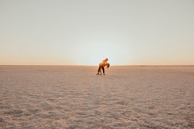 Rear view of woman walking at beach against clear sky during sunset
