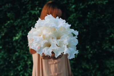 Woman showing white flowers while standing against plants