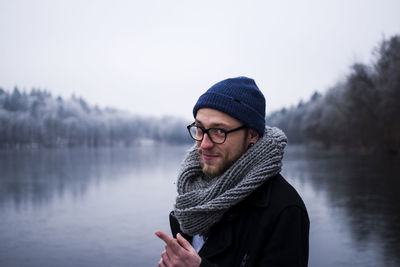 Portrait of young man standing against lake and sky during winter