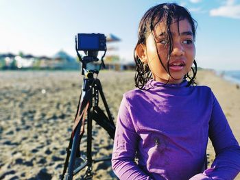 A girl is standing next to a camera tripod on the beach